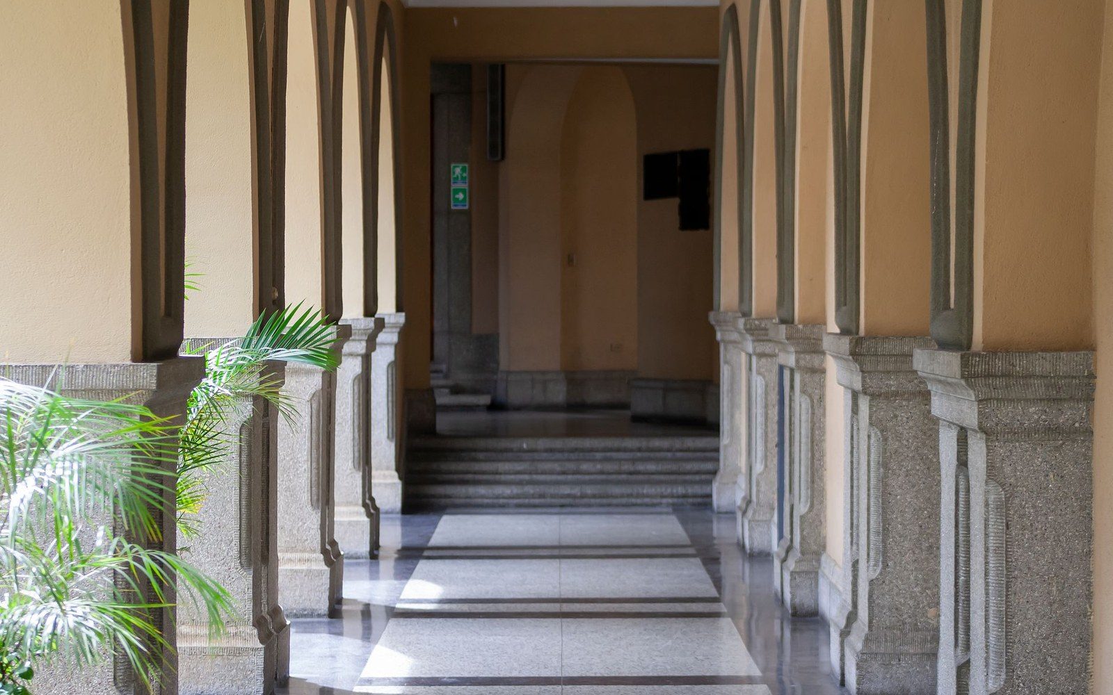 Arched colonnade with stone columns leads to a staircase and green exit sign